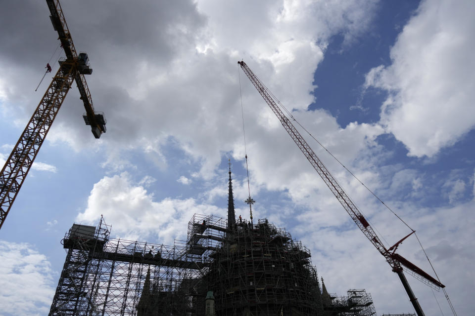 Workers install Notre Dame de Paris cathedral's Croix du Chevet in front of the cathedral spire, left, to be reinstalled Friday, May 24, 2024, in Paris. The Croix du Chevet is the only piece of the cathedral roof that did not burn in the devastating April 2019 fire. (AP Photo/Thibault Camus)