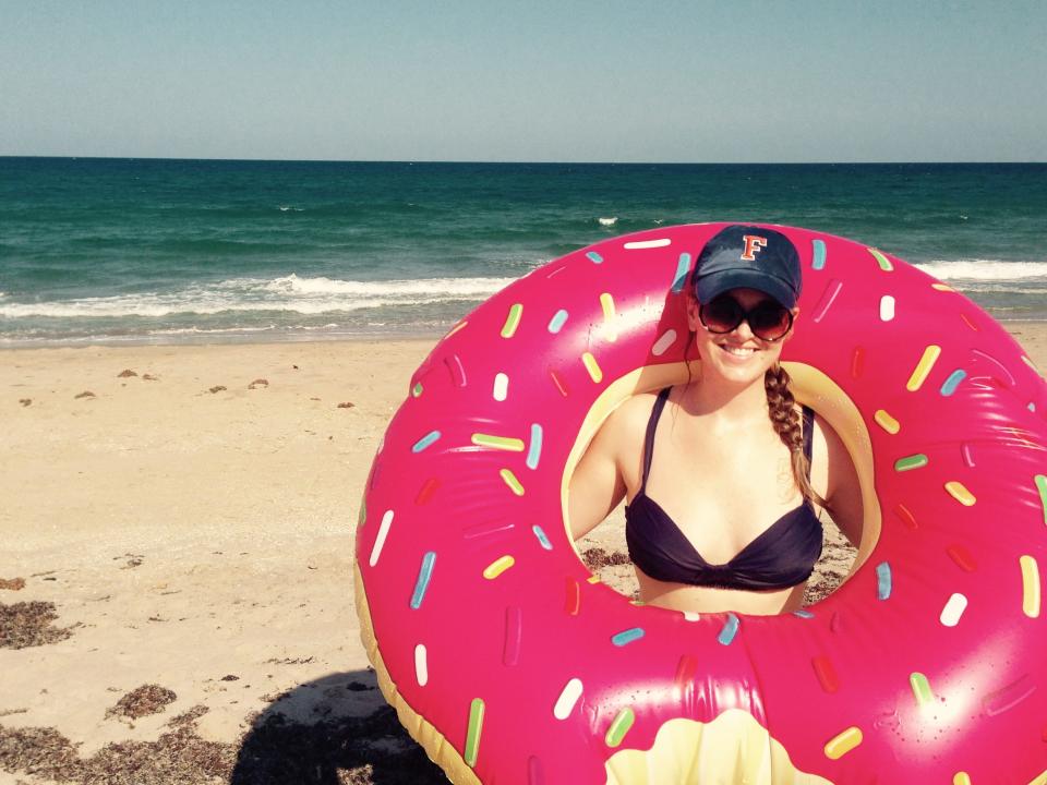 A woman on a beach wearing a baseball cap posing in a donut-style floatie ring.