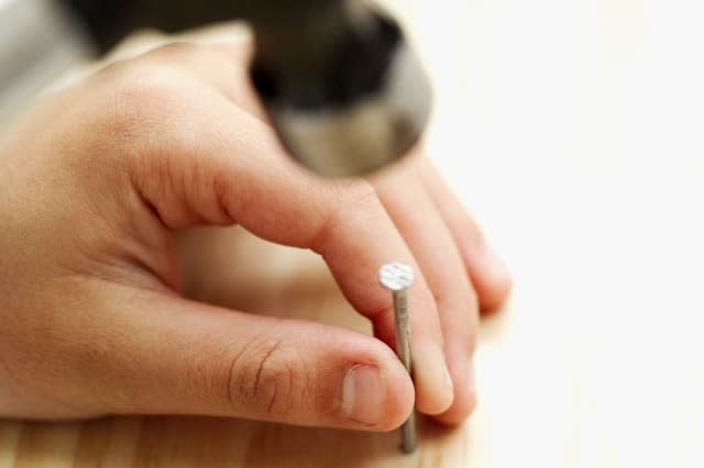 close-up of a boy about to hammer a nail into wood