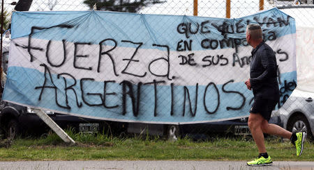 A man jogs past a banner in the colours of the Argentine national flag in support of the 44 crew members of the missing at sea ARA San Juan submarine, placed on a fence at an Argentine naval base in Mar del Plata, Argentina November 22, 2017. Words on the flag read "We are with you". REUTERS/Marcos Brindicci