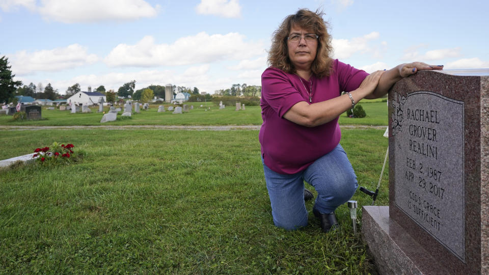 Sharon Grover rests her hands on the gravestone for her daughter, Rachael, Tuesday, Sept. 28, 2021, at Fairview Cemetery in Mesopotamia, Ohio. Grover believes her daughter started using prescription painkillers around 2013 but missed any signs of her addiction as her daughter, the oldest of five children, remained distanced. (AP Photo/Tony Dejak)