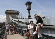 In this photo taken on Wednesday, June 5, 2019, tourists and Hungarians walk on the Chain Bridge over the Danube River in Budapest. A tourism boom in the Hungarian capital has led to major congestion on the river flowing through the city, with sightseeing boats and floating hotels competing for better positions in front of spectacular neo-Gothic buildings, ornate bridges and churches lining the Danube. (AP Photo/Laszlo Balogh)