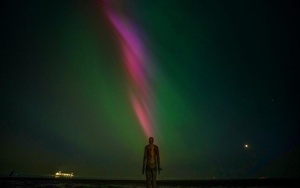 The aurora borealis, also known as the northern lights, glow on the horizon at Another Place by Anthony Gormley, Crosby Beach, Liverpool , Merseyside
