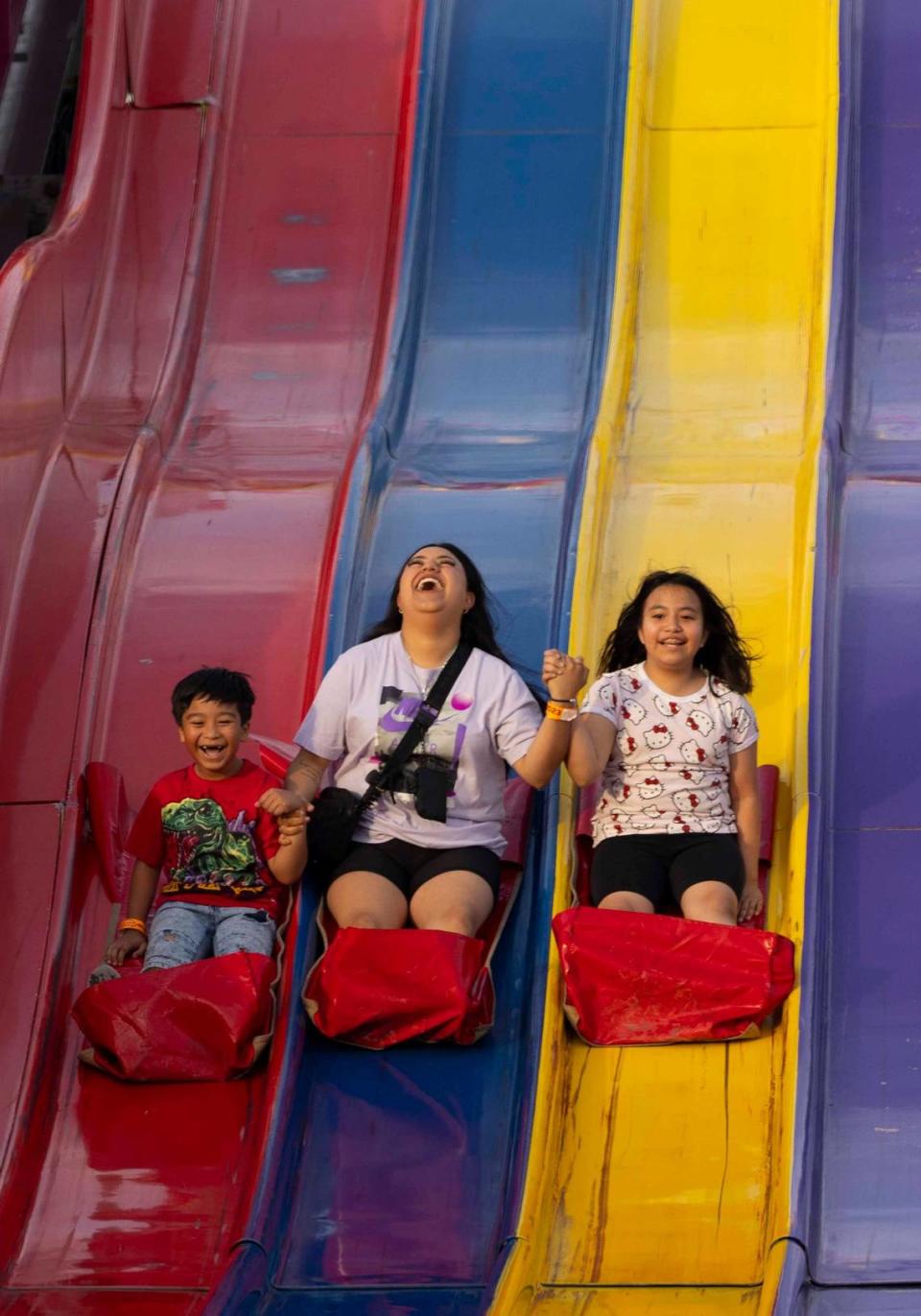 Jennifer Guillen, center, rides down the slide with Hano Andrade, left, and his sister, Athena, during the Youth Fair opening day on Thursday, March 14, 2024, at the Miami-Dade Fair and Exposition.