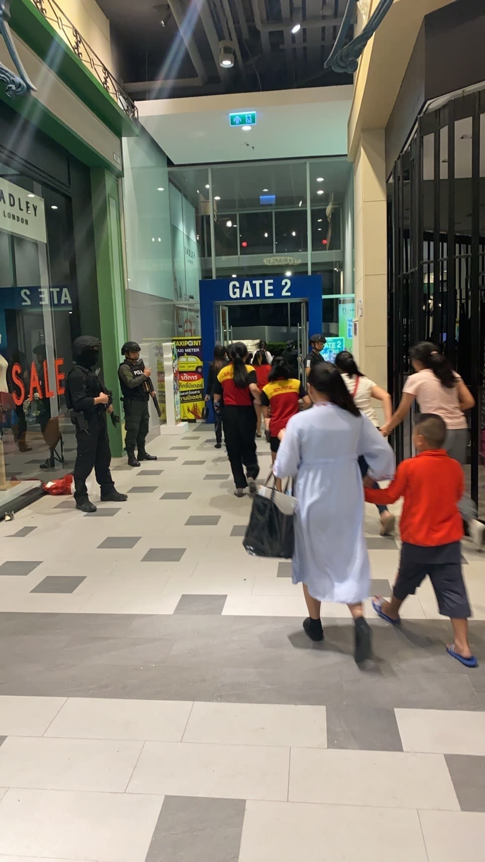 In this photo made available by the Crime Suppression Division, people are seen heading to an exit of the Terminal 21 Korat mall guarded by armed police in Korat, Thailand, Saturday, Feb. 8, 2020. A soldier shot multiple people in northeastern Thailand on Saturday, killing at least 16, and was holed up in a popular shopping mall, an emergency worker said. (Crime Suppression Division of The Royal Thai Police via AP)