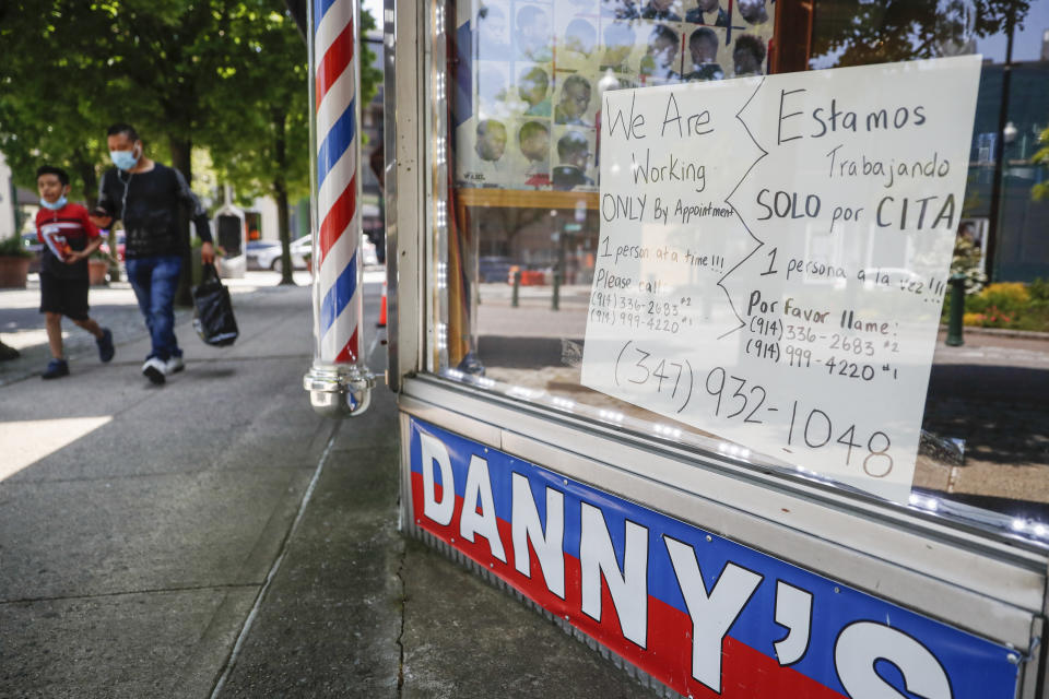 Pedestrians pass a barbershop that displays a sign advertising haircuts by appointment only, Tuesday, May 26, 2020, in New Rochelle, N.Y. (AP Photo/John Minchillo)