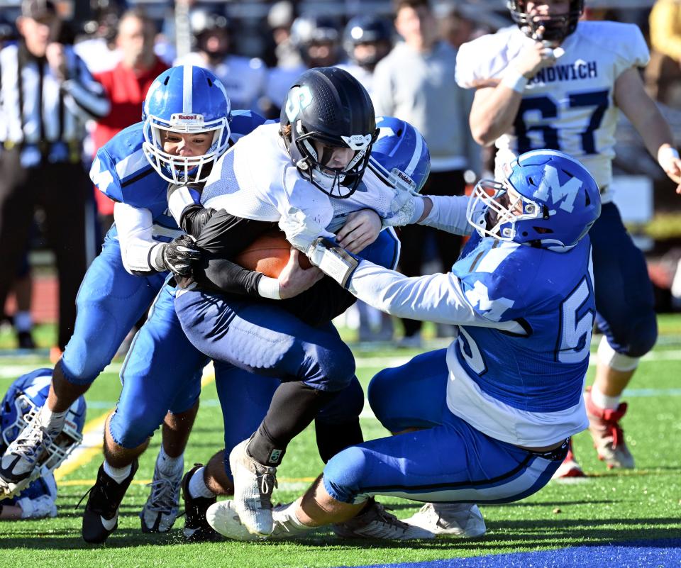 Sandwich quarterback Adam Ferreira is dragged down by Mason Zylinski (right) and Coti Weeden of Mashpee.