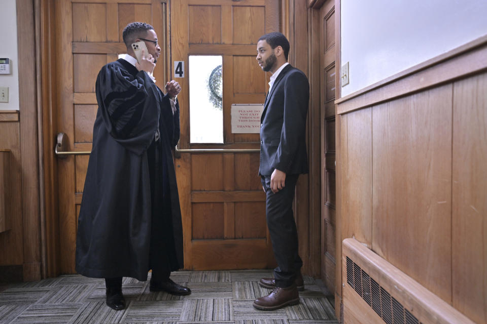 The Rev. Brandon Thomas Crowley, left, takes a phone call to deal with a last minute concern as parishioner Mark Kendall, right, looks on in a vestibule just before Sunday service at Myrtle Baptist Church in Newton, Mass., on Sunday, May 5, 2024. (AP Photo/Josh Reynolds)