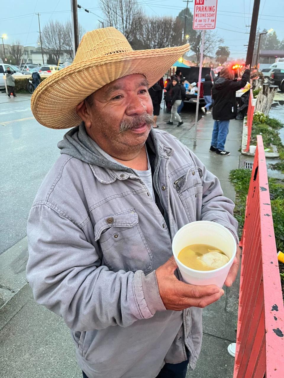 A man in a jacket and hat holds a foam container of soup.