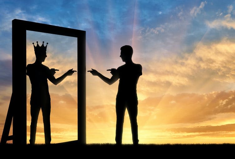 Silhouette of a man pointing at himself at the mirror, his reflection wearing a crown.