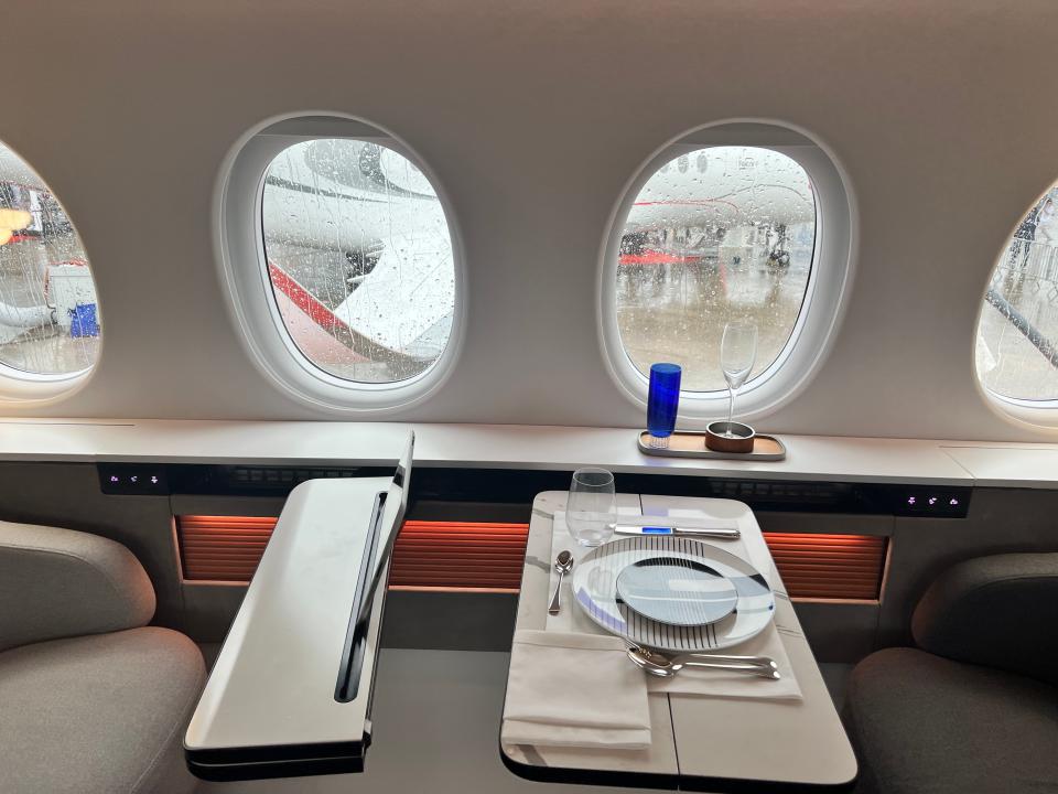 Two foldout tables, one with a plate and cutlery set out, on board a Falcon 10X with four windows in the background