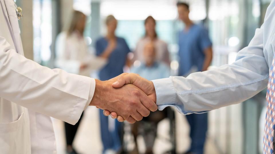 Close up of unrecognizable doctor and insurance agent handshaking - Incidental people at background.