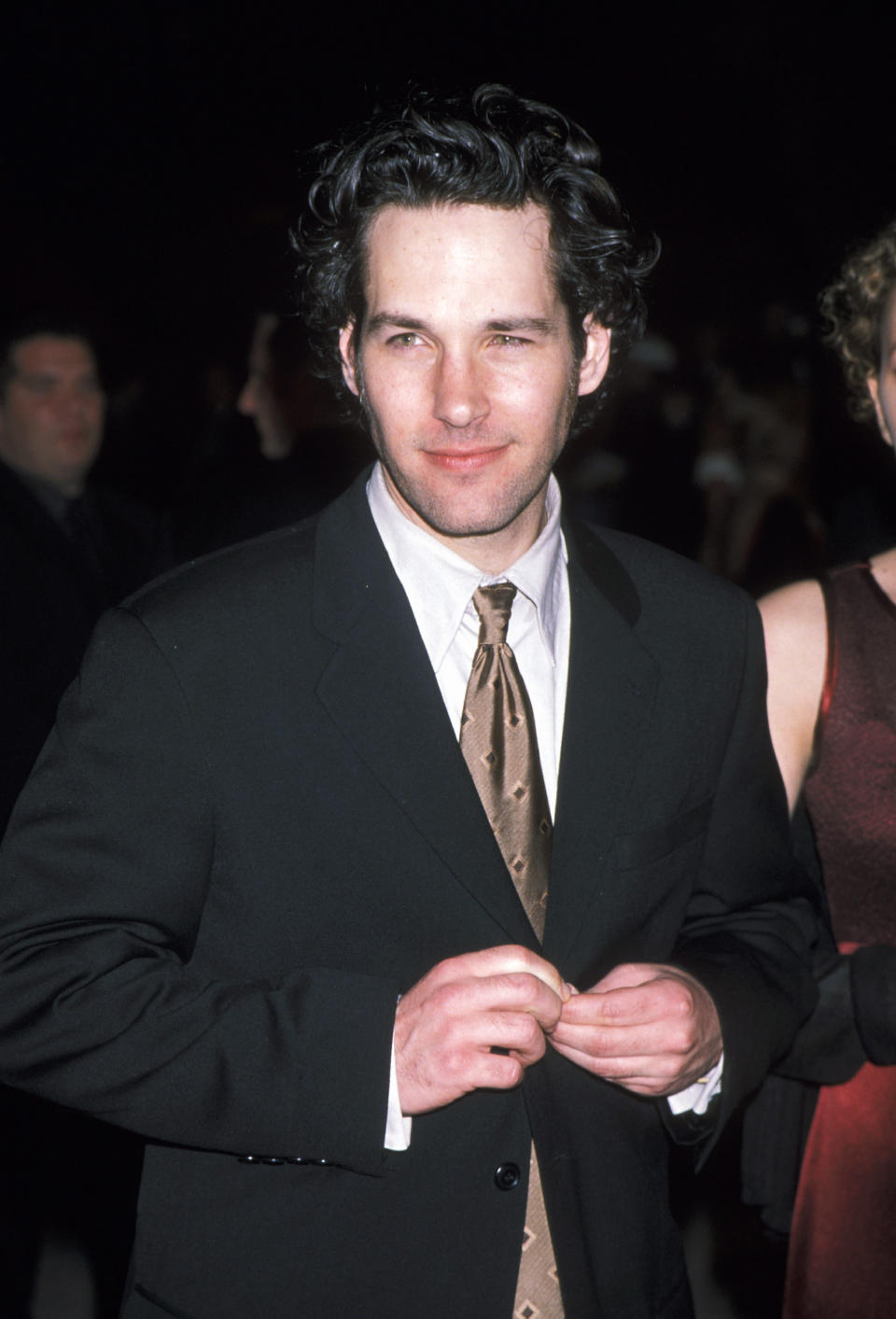 Man buttoning suit jacket, wearing tie. Facial expression is a gentle smile