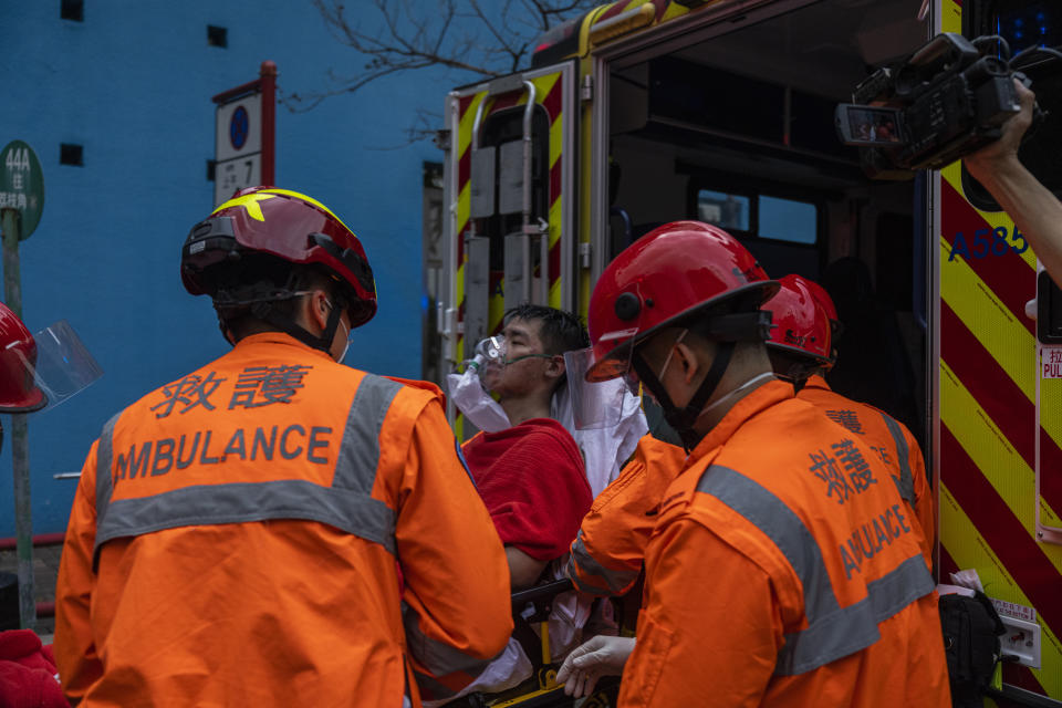 Ambulance staff attend a patient nearby the fire site in Cheung Sha Wan, a residential and industrial area, in Hong Kong, Friday, March 24, 2023. Hong Kong firefighters were battling a blaze Friday at a warehouse that forced more than 3,000 people to evacuate, including students, police said. (AP Photo/Louise Delmotte)