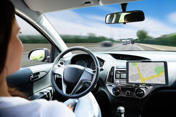 Woman in a car with steering wheel, dashboard, and GPS screen visible; vehicle in motion on a road