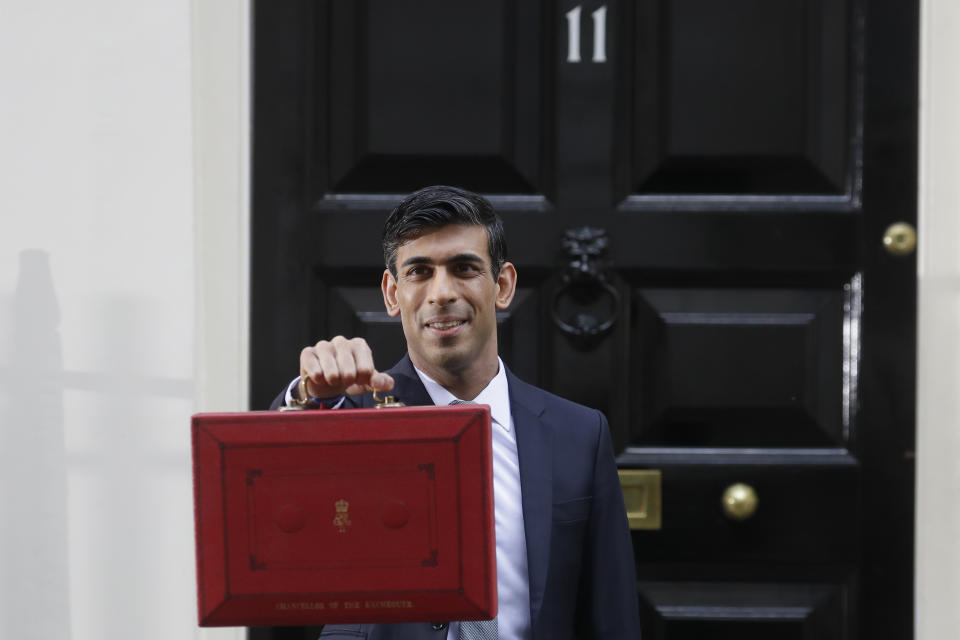 Britain's Chancellor of the Exchequer Rishi Sunak stands outside No 11 Downing Street and holds up the traditional red box that contains the budget speech for the media, he will then leave to make budget speech to House of Commons, in London, Wednesday, March 11, 2020. Britain's Chancellor of the Exchequer Rishi Sunak will announce the first budget since Britain left the European Union. (AP Photo/Kirsty Wigglesworth)