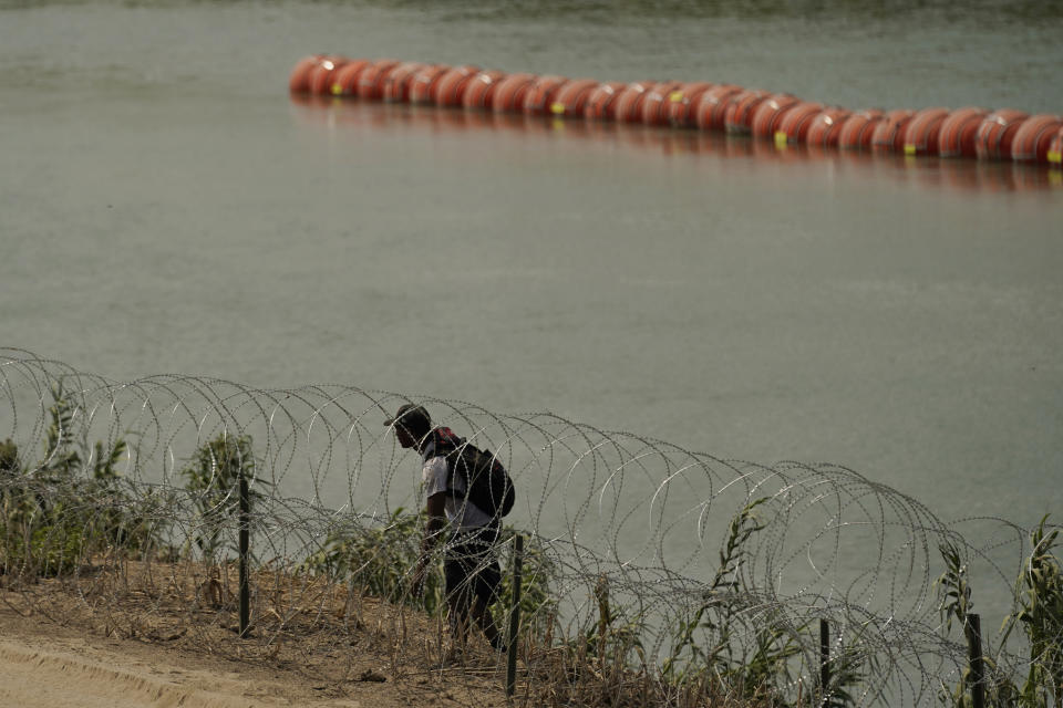 A migrant from Columbia walks along Concertina wire and a floating buoy barrier after crossing the Rio Grande from Mexico into the U.S., Monday, Aug. 21, 2023, in Eagle Pass, Texas. (AP Photo/Eric Gay)