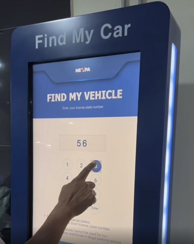 Interactive kiosk screen with "Find My Vehicle" feature engaged, a finger entering a license plate number