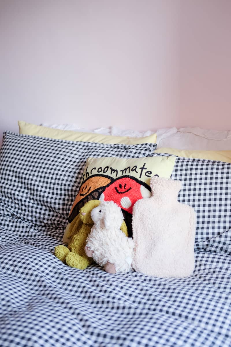 Stuffed animals sit on gingham bedding in pink bedroom.