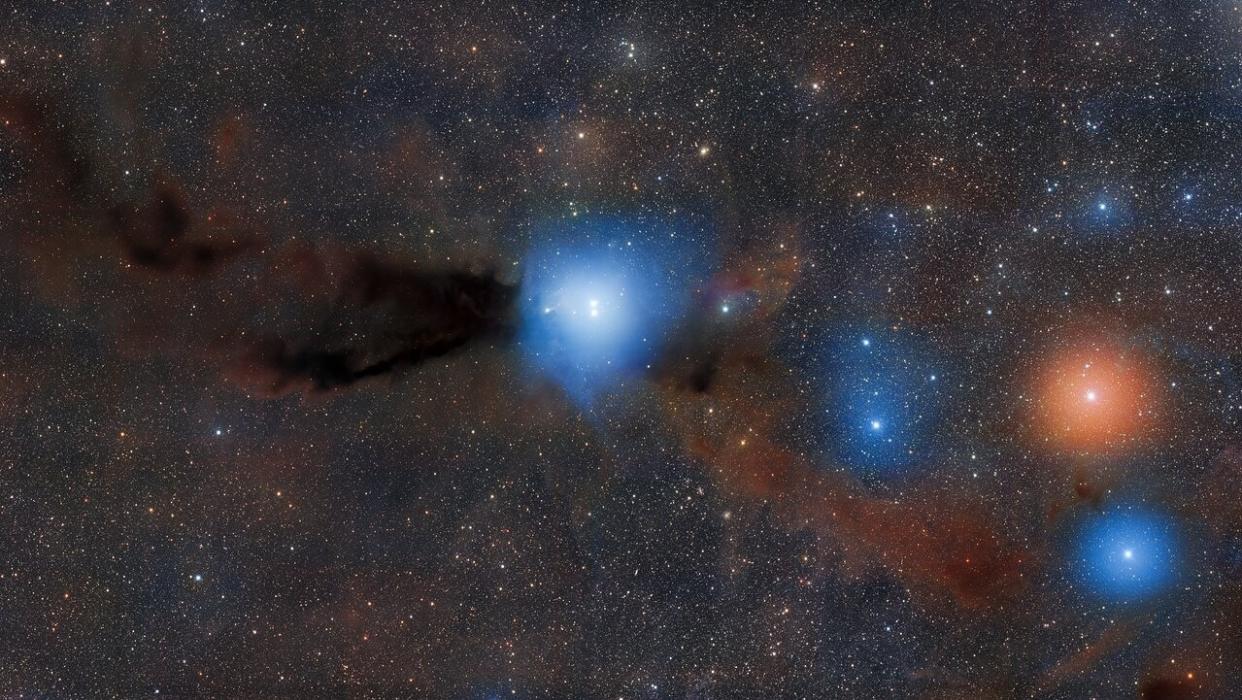 two bright spheres of light in the center of the image are surrounded by a hazy blue glow, piercing through a dark cloud of gas and dust.  