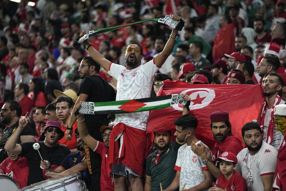 A fan holds a flag of Palestine as he cheers for the national team of Tunisia during the World Cup group D soccer match between Denmark and Tunisia, at the Education City Stadium in Al Rayyan, Qatar, Tuesday, Nov. 22, 2022. (AP Photo/Ariel Schalit)