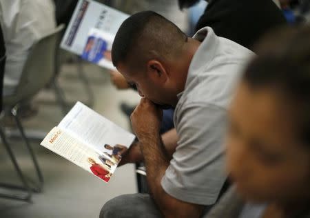 People read pamphlets as they wait in line at a health insurance enrollment event in Cudahy, California March 27, 2014. REUTERS/Lucy Nicholson