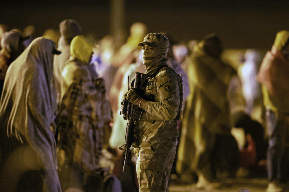 A Texas National Guard soldier provides security around migrants gathered around a gate in the border fence in El Paso, Texas, in the early hours of Thursday, May 11, 2023. Migrants rushed across the border hours before pandemic-related asylum restrictions were to expire Thursday, fearing that new policies would make it far more difficult to gain entry into the United States. (AP Photo/Andres Leighton)