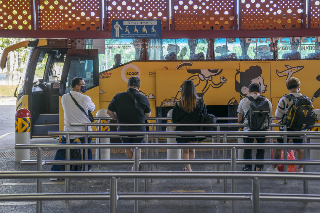 Singapore, Singapore - November 29, 2021: A row of people wait at Woodlands Temporary Bus Interchange to board a coach bus headed for Johor Bahru in Malaysia. The buses were travelling on the first day of a Vaccinated Travel Lane (VTL) scheme launched by the two countries.