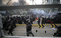 Riot police officers are seen through the smashed window of a bus station during a clash with student protesters in Jakarta, Indonesia, Thursday, Oct. 8, 2020. Thousands of enraged students and workers staged rallies across Indonesia on Thursday in opposition to the new law they say will cripple labor rights and harm the environment. (AP Photo/Dita Alangkara)