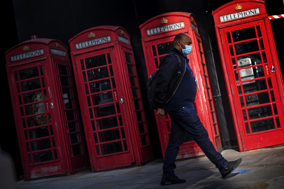 A man wearing a face covering walks past a row of red telephone boxes in Westminster, London, after a range of new restrictions to combat the rise in coronavirus cases came into place in England.