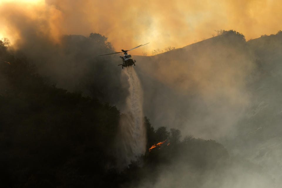 A firefighting helicopter drops water onto a brush fire scorching at least 100 acres in the Pacific Palisades area of Los Angeles on Saturday, May 15, 2021. (AP Photo/Ringo H.W. Chiu)