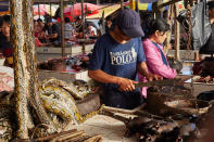 A market trader slicing up fruit bats is surrounded by his other wildlife wares: pythons to his right, with bamboo-skewered ‘bush’ rats beneath them.