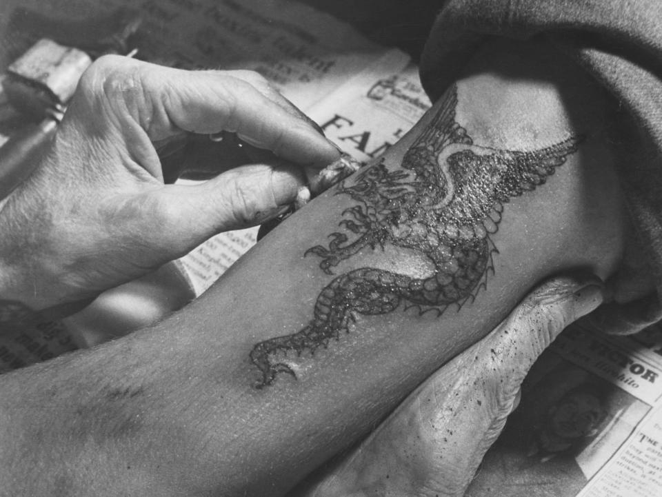 British tattooist George Burchett applies a Chinese dragon tattoo to an arm