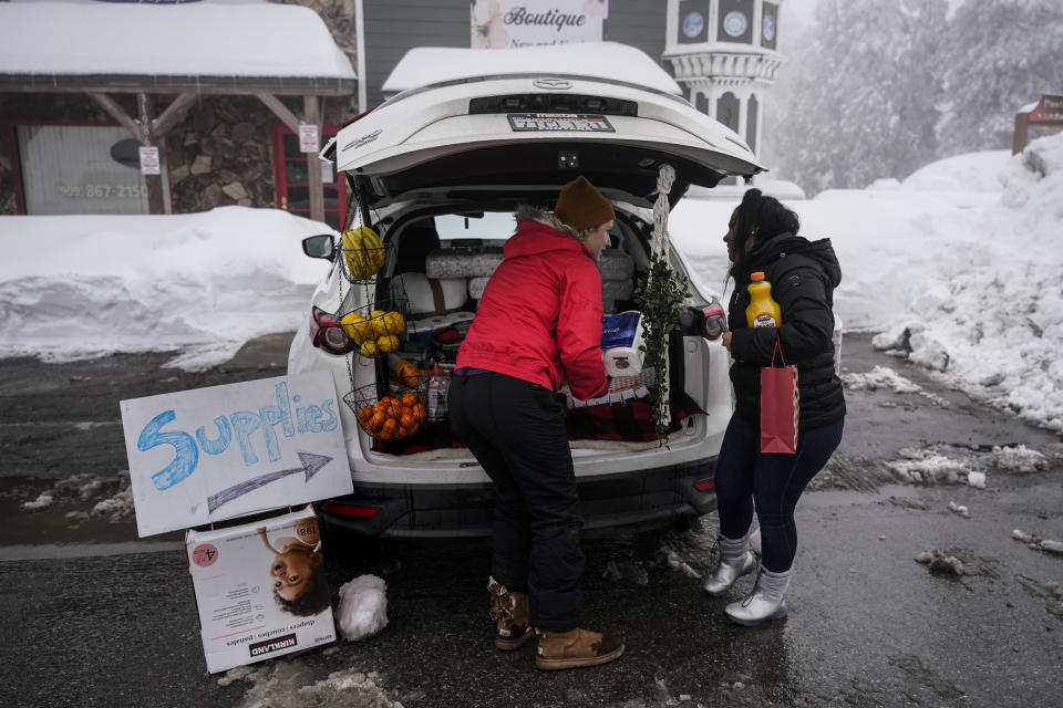 Ruth Aldama, center, who set up a makeshift supply shop on the road, talks to a resident in Running Springs , Calif., Tuesday, Feb. 28, 2023. Beleaguered Californians got hit again Tuesday as a new winter storm moved into the already drenched and snow-plastered state, with blizzard warnings blanketing the Sierra Nevada and forecasters warning residents that any travel was dangerous. (AP Photo/Jae C. Hong)