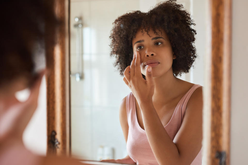 Woman with curly hair applying face cream, looking at herself in the mirror