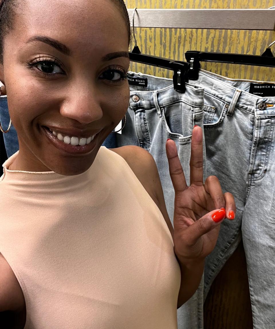 Author Joi-Marie McKenzie posing next to a rack of jeans in a Nordstrom dressing room.