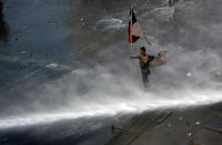 Holding a Chilean flag, a protester braces against a water canon sprayed from a police truck amid a march by students and union members in Santiago, Chile, Monday, Oct. 21, 2019. Protesters defied an emergency decree and confronted police in Chile’s capital on Monday, continuing disturbances that have left at least 11 dead and led the president to say the country is “at war.” (AP Photo/Miguel Arenas)