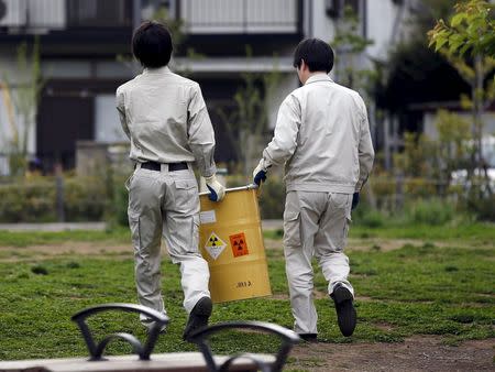 Workers of Tokyo's Toshima ward office carry away a container holding a fragment of an unknown object after it was dug up from the ground near playground equipment at a park in Toshima ward, Tokyo April 24, 2015. REUTERS/Toru Hanai