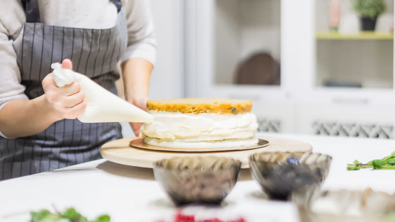 person frosting cake with piping bag