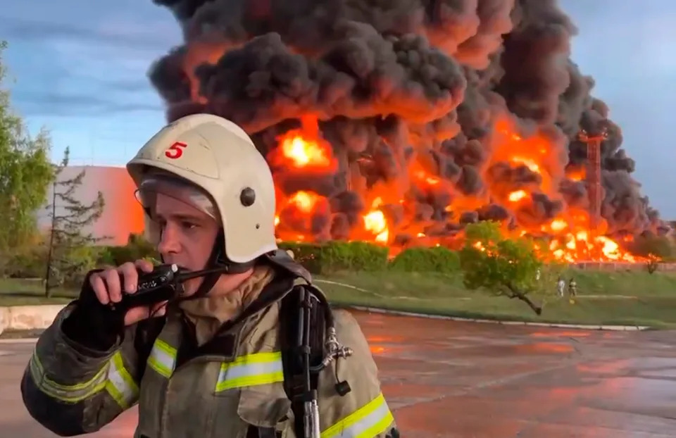 In this handout photo made from video released by the governor of Sevastopol, Mikhail Razvozhaev, on April 29, 2023, on Telegram, a firefighter speaks on a walkie-talkie as smoke and flames rise from a burning fuel tank in Crimea.