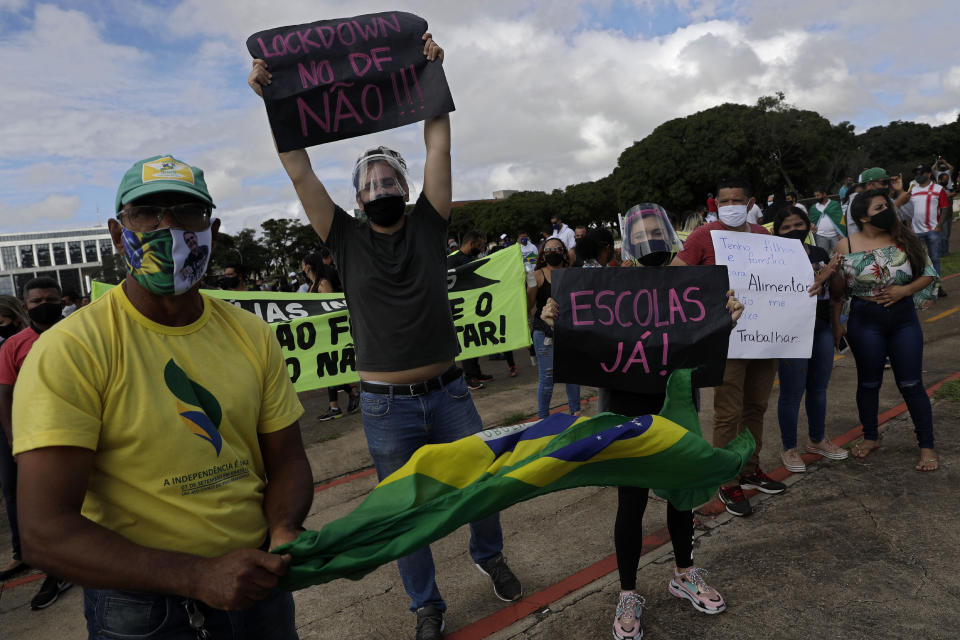 Demonstrators hold up Portuguese messages like "No lockdown!" and "Schools now!" on the first day of a two-week-long lockdown to curb the spread of COVID-19 in Brasilia, Brazil, Monday, March. 1, 2021. It’s the second lockdown since the start of the pandemic one year ago. (AP Photo/Eraldo Peres)