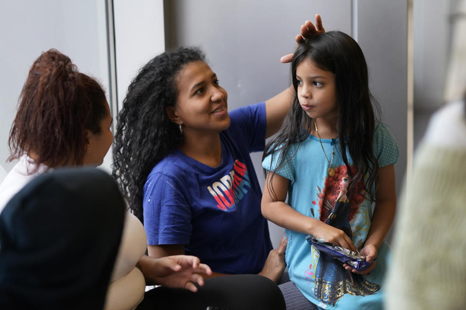 Karen Malave, center, an immigrant from Venezuela, smiles as she fixes her daughter Avril Brandelli's hair, while they and other families take shelter in the Chicago Police Department's 16th District station Monday, May 1, 2023. Chicago has seen the number of new arrivals grow tenfold in recent days. Shelter space is scarce and migrants awaiting a bed are sleeping on floors in police stations and airports. (AP Photo/Charles Rex Arbogast)