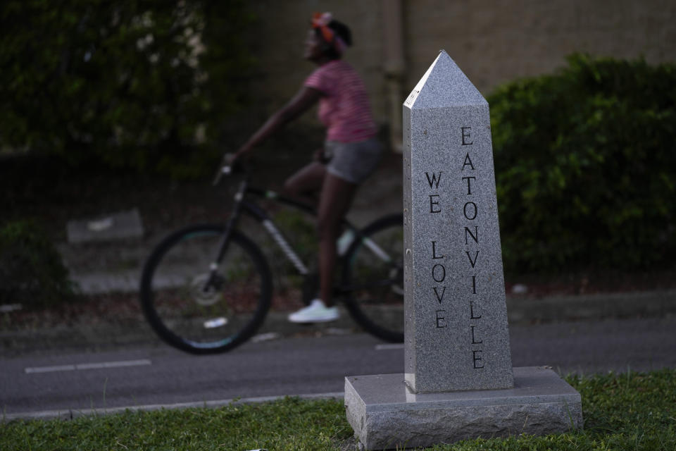 A woman bikes past a monument on the main boulevard running through Eatonville, Fla., Tuesday, Aug. 22, 2023. In Florida, one of the first incorporated self-governing Black municipalities in the United States was Eatonville, established in 1887. Located just 24 miles (39 kilometers) north of Disney World, the key challenge for present-day residents is the Orange County Public School Board, which owns 100 acres (40 hectares) of property in the middle of town. (AP Photo/Rebecca Blackwell)