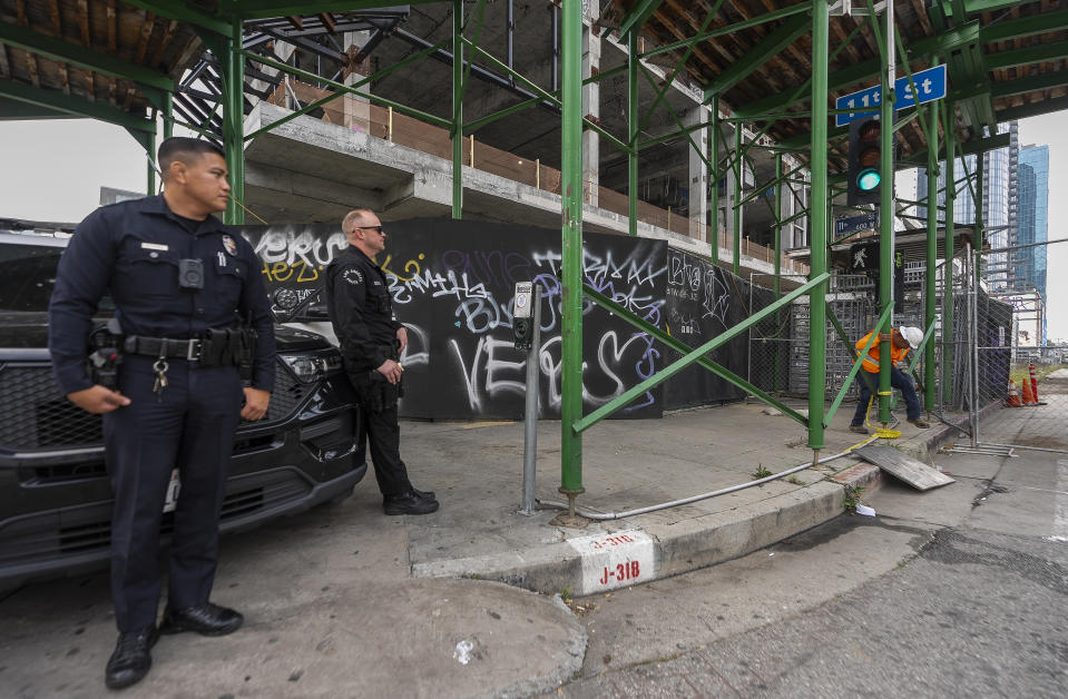 Los Angeles Police officers guard the exterior of an unfinished complex of high-rise towers that have recently been vandalized with graffiti and used for dangerous social media stunts after the developer ran out of money is seen in downtown Los Angeles Friday, Feb. 16, 2024. The three towers have become an embarrassment in a high-profile area that includes Crypto.com Arena, home of major sports teams and events such as the Grammys, as well as the Los Angeles Convention Center and the L.A. Live dining and events complex. (AP Photo/Damian Dovarganes)