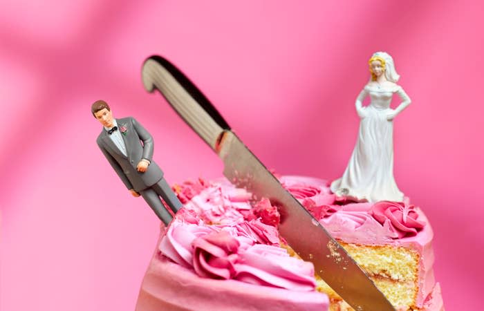 Wedding cake topper with bride and groom figurines; knife slicing into the cake