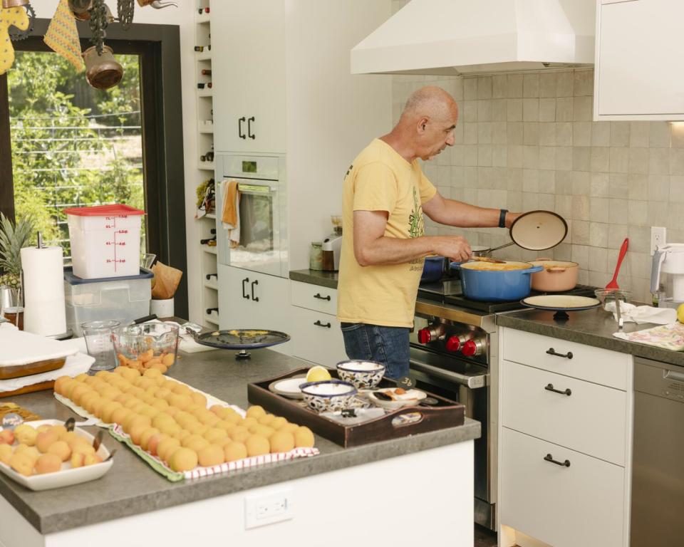 Amer Budayr boils apricots. More apricots are on the kitchen counter behind him.