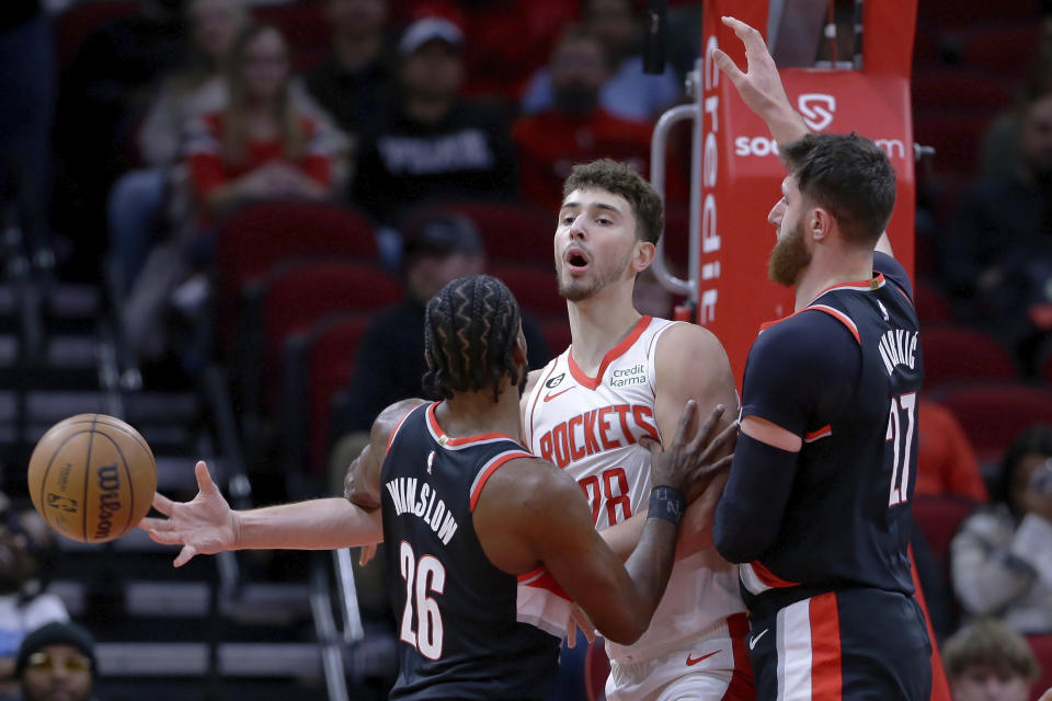 Houston Rockets center Alperen Sengun, center, passes the ball around Portland Trail Blazers forward Justise Winslow (26) and center Jusuf Nurkic, right, during the first half of an NBA basketball game Saturday, Dec. 17, 2022, in Houston. (AP Photo/Michael Wyke)