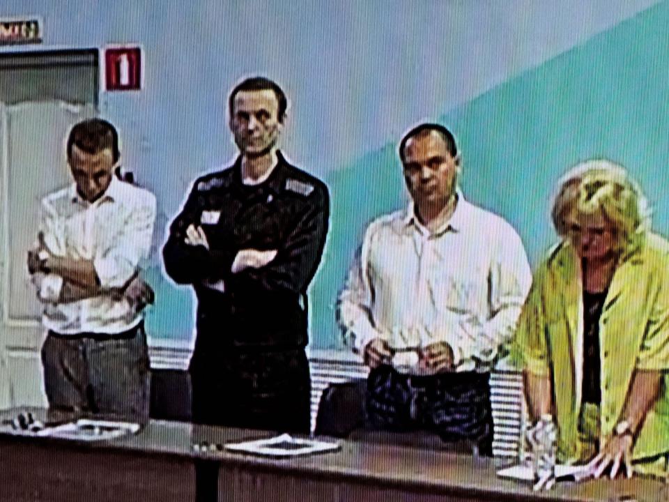 A screen shows Alexei Navalny and others standing in front of a desk.