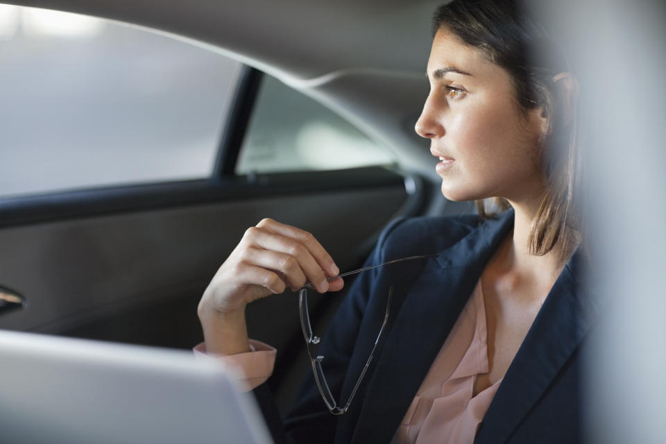 Pensive businesswoman with laptop in back seat of car
