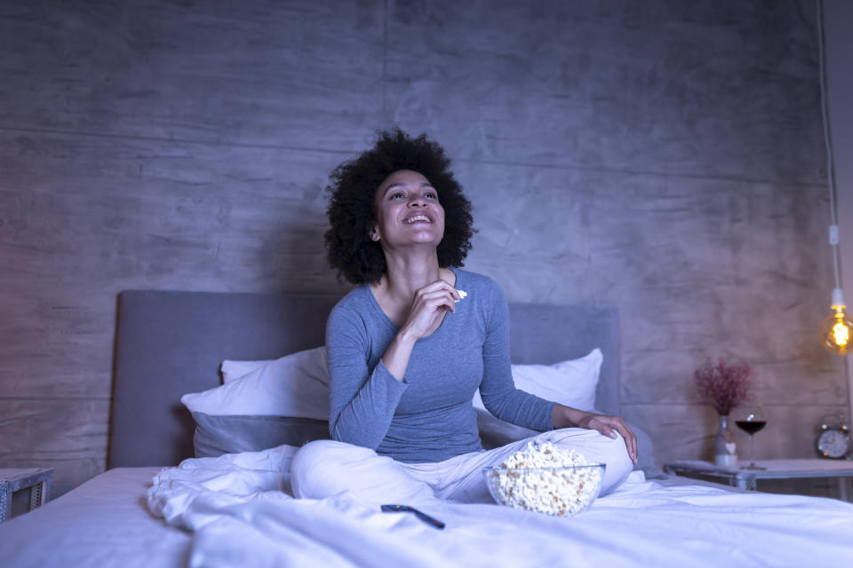 a person in bed eating popcorn and watching tv